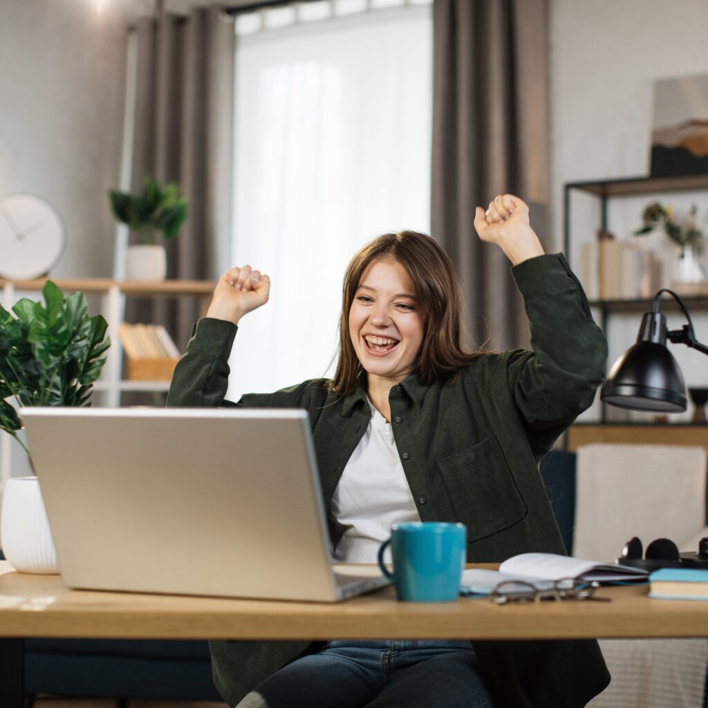 girl raising hands in celebration while looking at her laptop